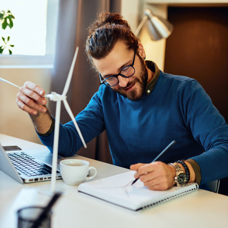 Man sitting at a desk writing on a pad with a model of a wind turbine in front of him