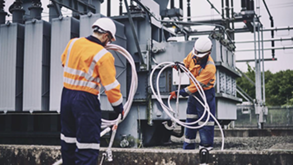 Two engineers wearing PPE coiling earth wires next to an electricity transformer